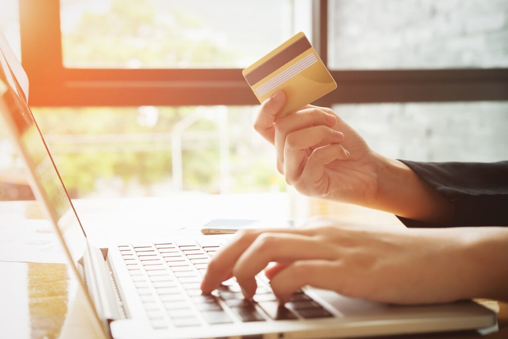Uma mão usando notebook, a outra segurando um cartão dourado, mesma cor do cartão de crédito BCP Prestige