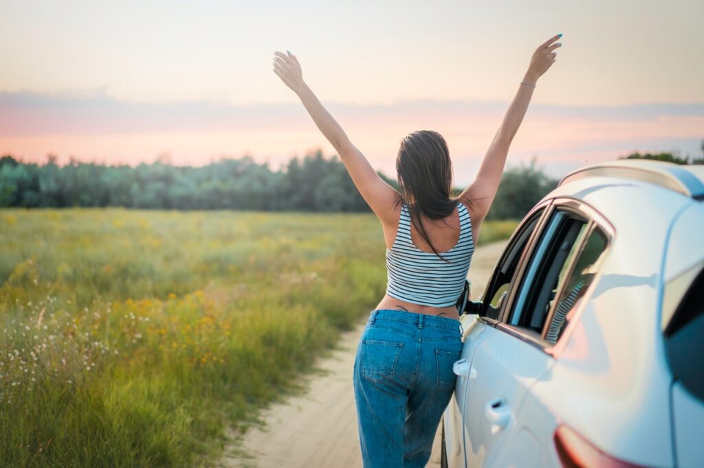 Mulher de braços abertos ao lado de carro em paisagem natural