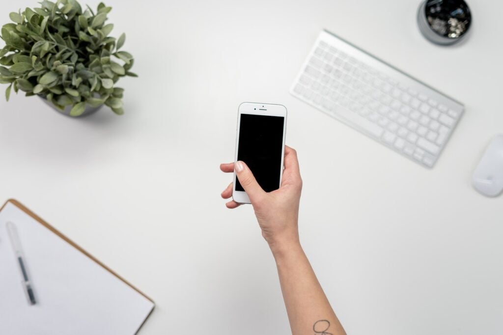Smartphone sendo segurado. Teclado de computador prancheta e planta sobre mesa.