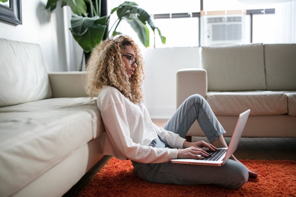 Mulher de óculos em sala usando notebook, encostada no sofá