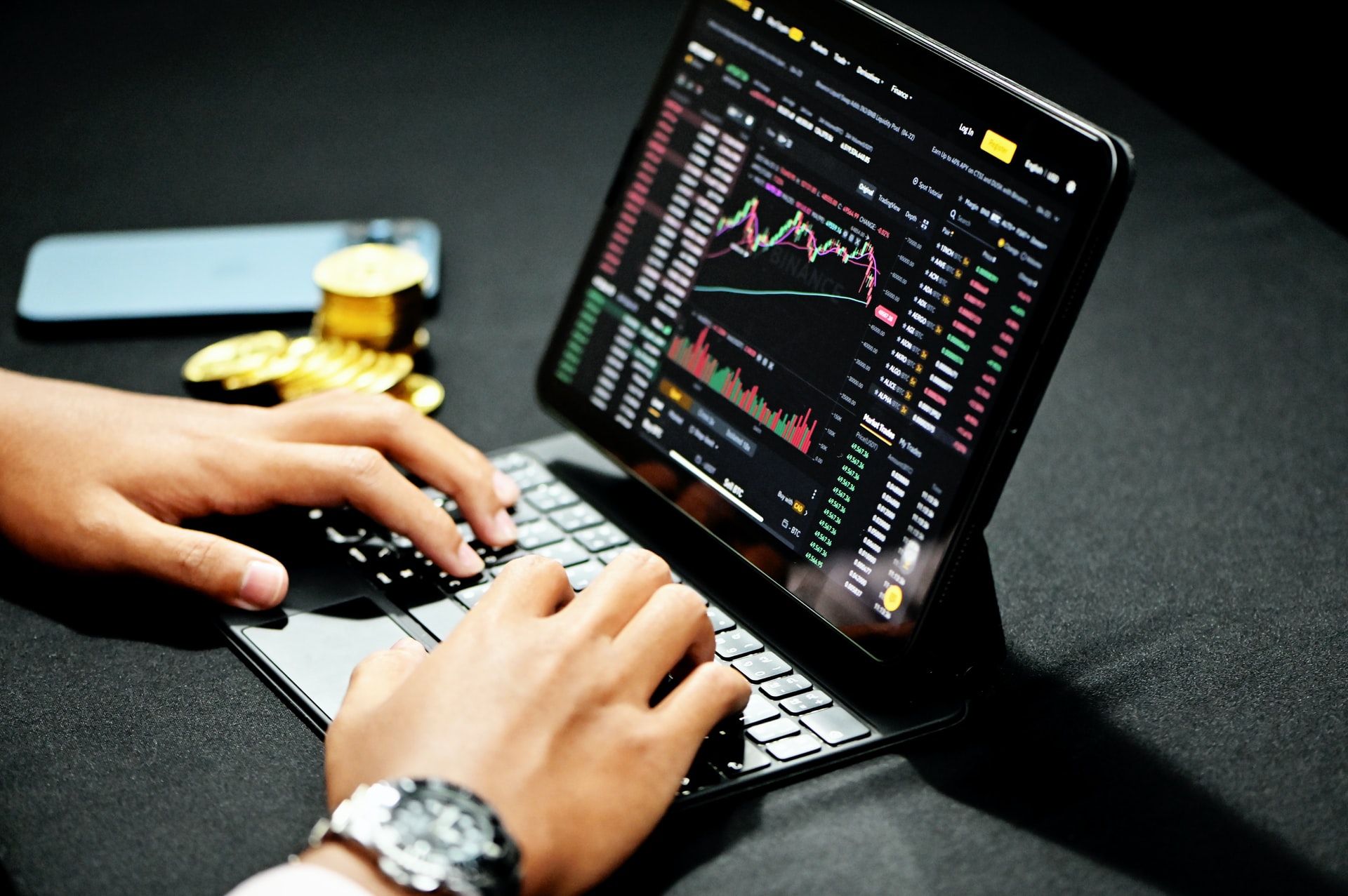 Celular, criptomoedas e mãos mexendo em tablet com corretora de criptomoedas na tela