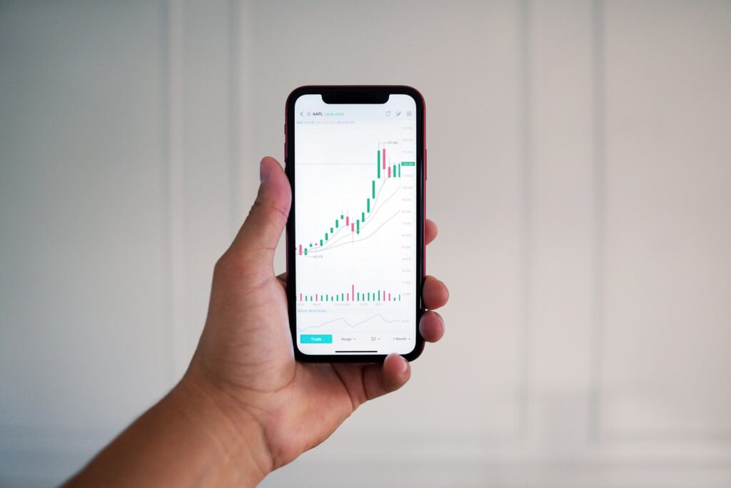 Mão segurando celular com tela mostrando corretora com gráficos de exchanges de cripto