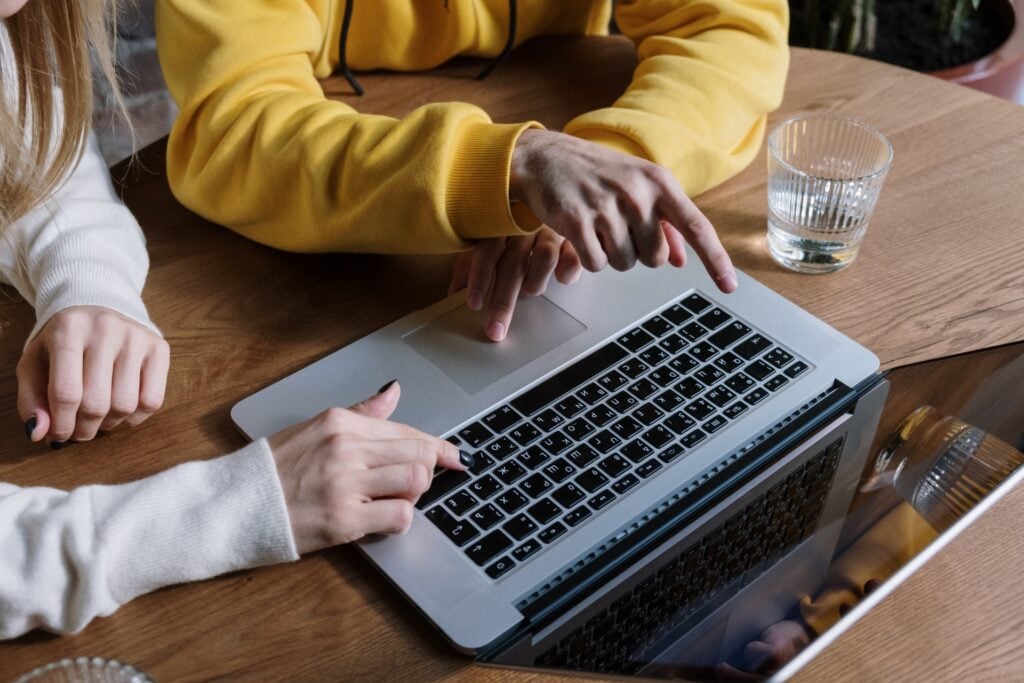 Duas pessoas apontando e usando notebook, copo de água sobre a mesa