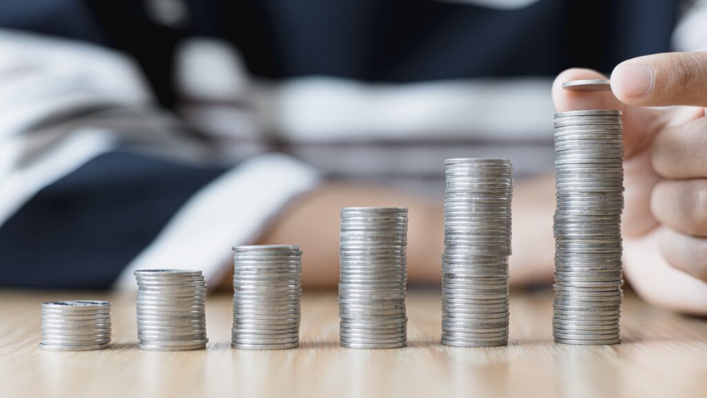 Moedas empilhadas em linha crescente, pessoa colocando moeda na coluna mais alta. Representando o dinheiro aumentando graças ao Crédito Consolidado Financial Liberty