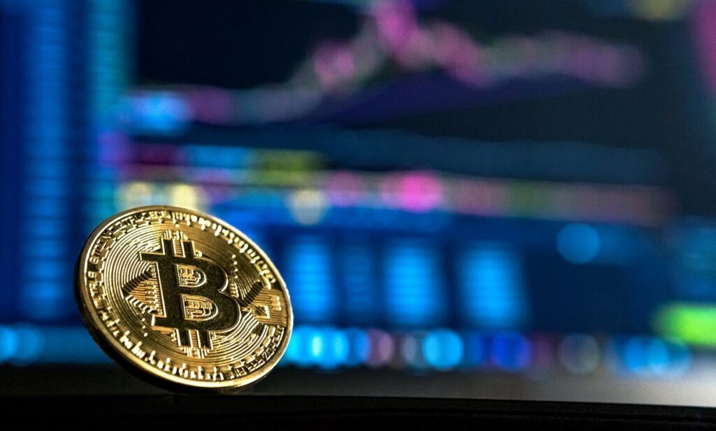 Bitcoin, criptomoeda disponível na corretora Bitcoin.com. Gráficos de transações digitais ao fundo.