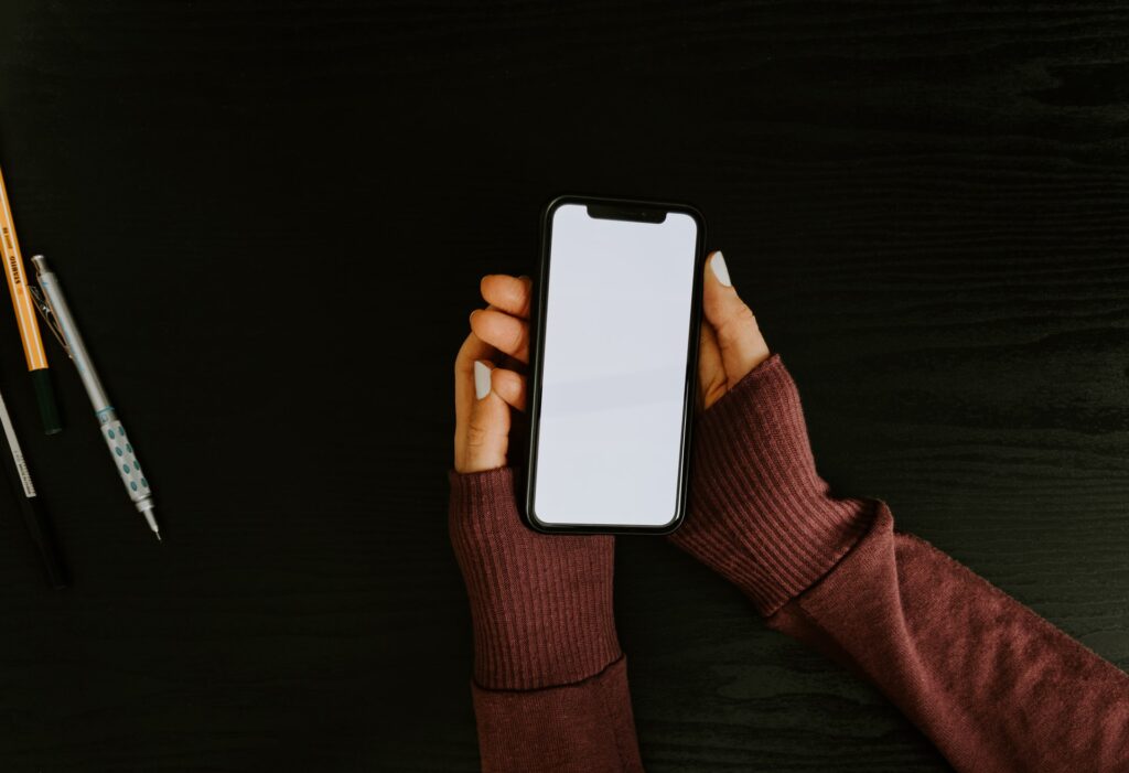 Fundo escuro com canetas. Mãos segurando celular, com o qual é possível fazer coisas como aderir à Skrill