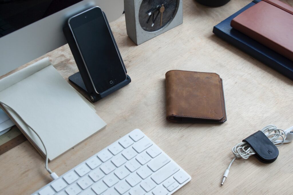 Sobre a mesa de escritório: relógio, agendas, fones, papel, teclado e monitor de computador, e celular. Simbolizando como aderir a XTB