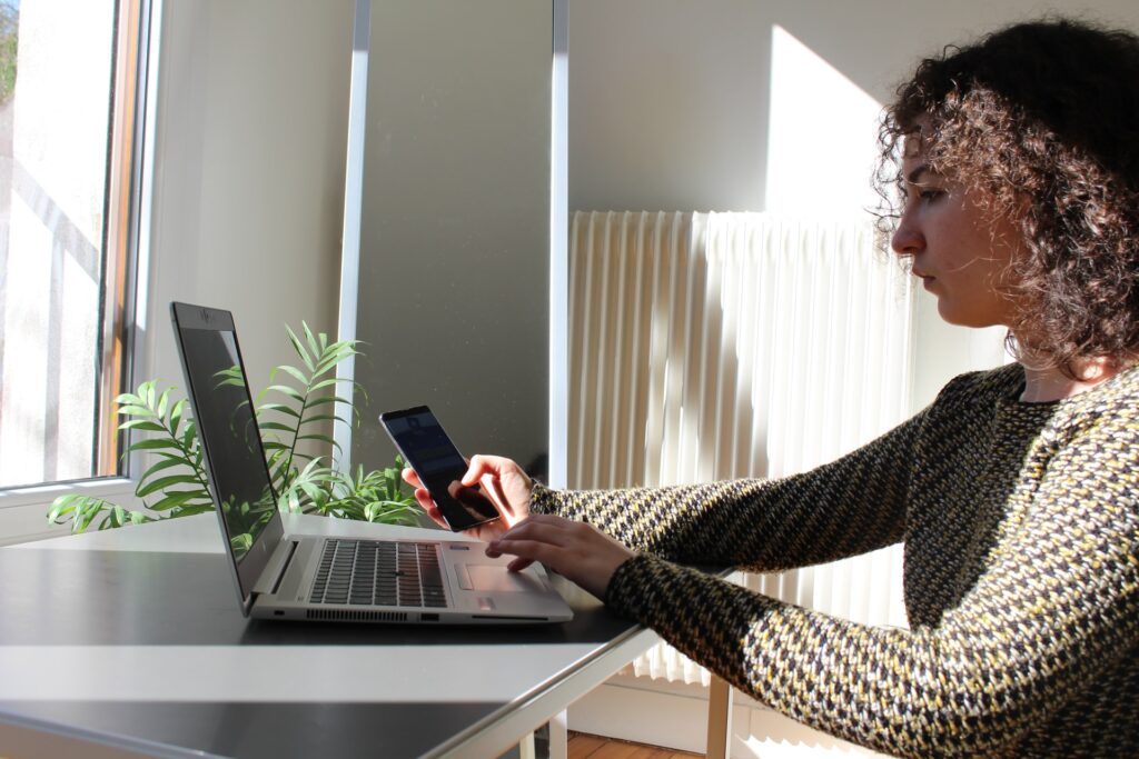 Jovem mulher usando notebook e mexendo em celular, representando como solicitar cartão de débito Jovem Novo Banco online