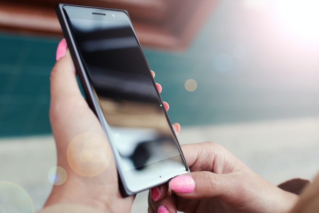 Mãos com unhas com esmalte rosa segurando smartphone, simbolizando como solicitar o cartão BCP Go! Changer online