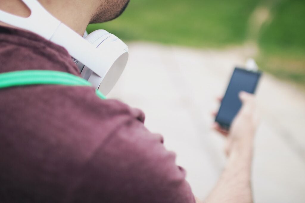 Homem com fones de ouvido pendurado no ombro, segurando celular. Simbolizando como solicitar crédito Cofidis