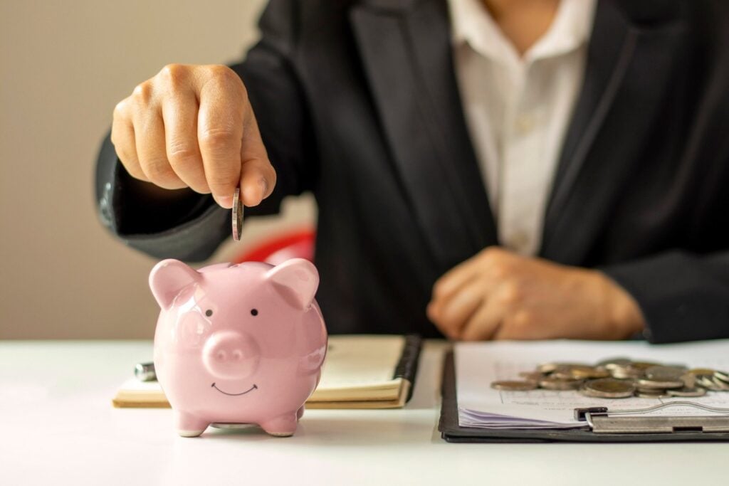 Pessoa de terno colocando moeda em cofrinho de porquinho, simbolizando o crédito consolidado Cifra7.
