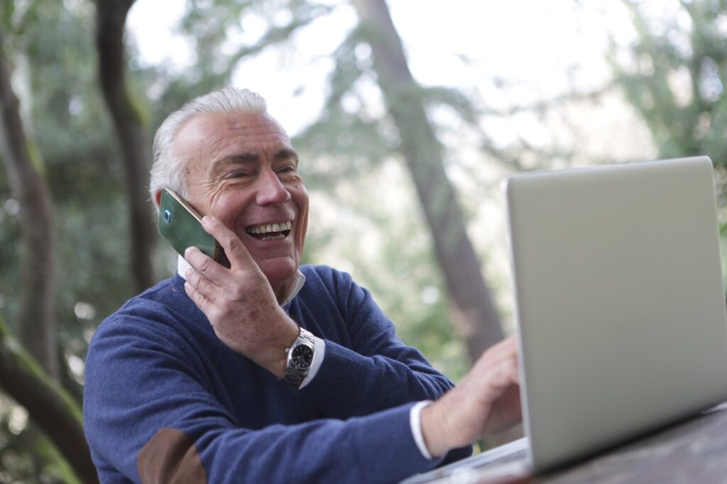 pessoa falando ao celular e sorrindo ao mesmo tempo em que mexe no computador