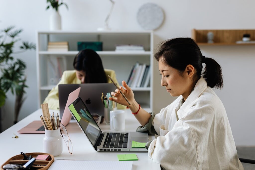 mulher japonesa com lápis entre os dedos em frente ao notebook fazendo pesquisa; ela também faz anotações em post its