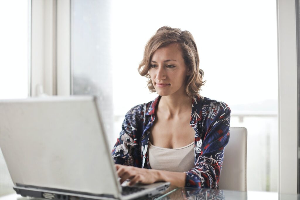 mulher sentada em cadeira com mesa mexendo no notebook