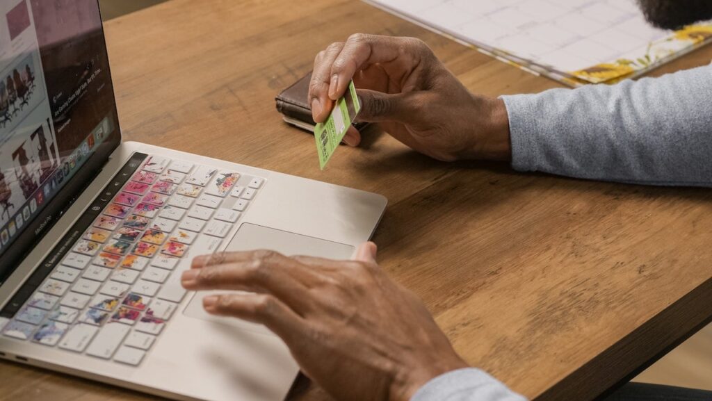 imagem de uma pessoa segurando um cartão de crédito em frente a um computador pesquisando sobre programa de pontos unibanco