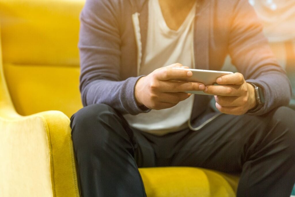 pessoa sentada em poltrona amarela segurando um celular