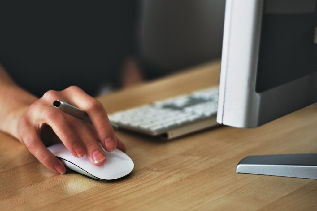 pessoa com uma caneta presa entre os dedos, mexendo no mouse e pesquisando pelo computador