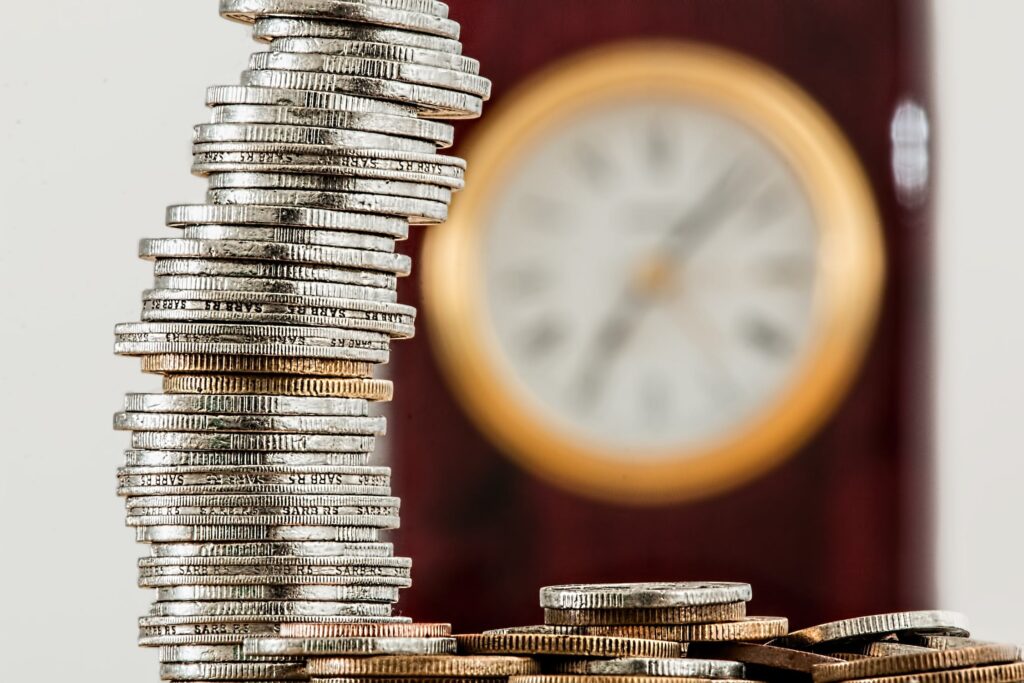 Pilha de moedas com relógio ao fundo