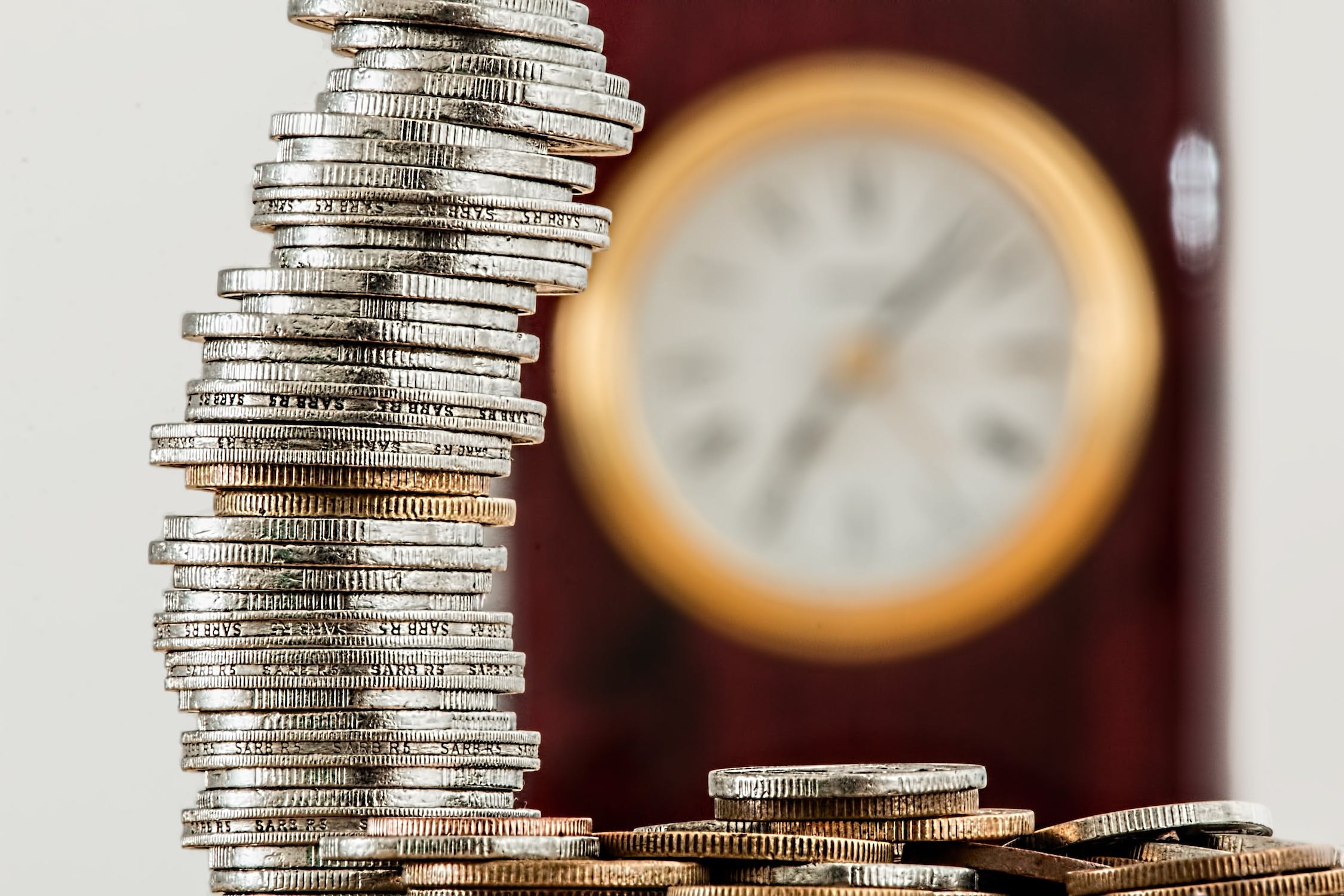 Pilha de moedas com relógio ao fundo