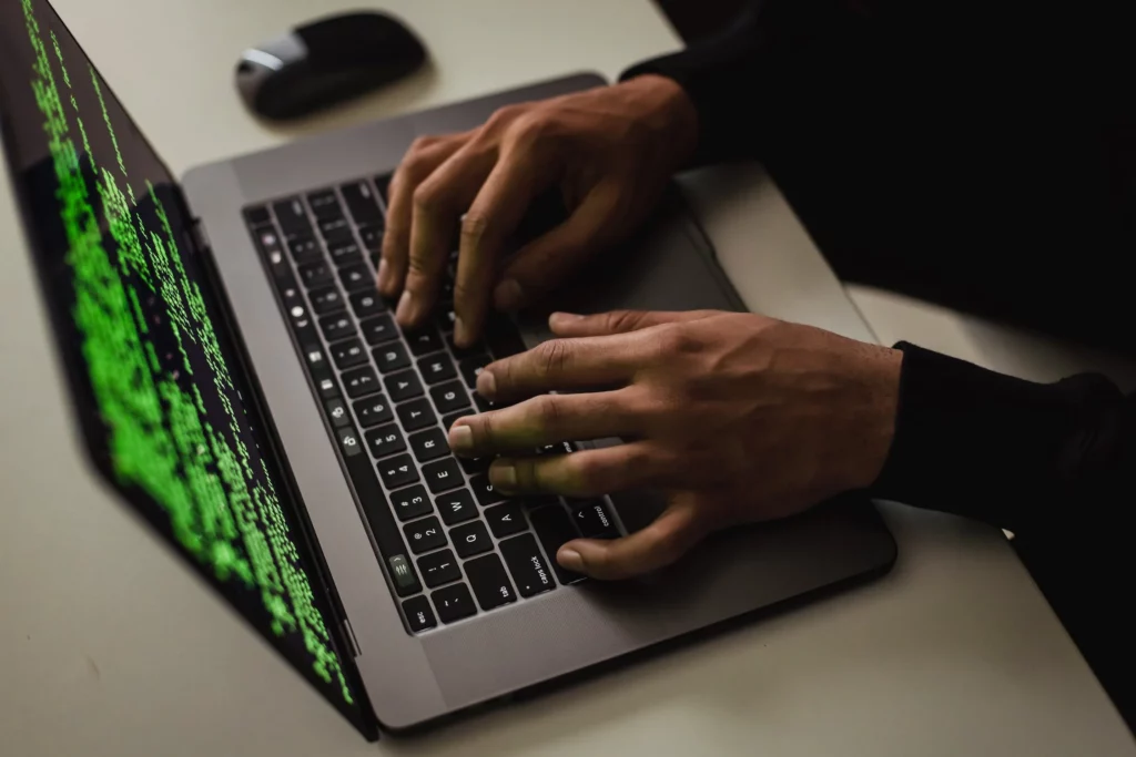Mão digitando em notebook com códigos na tela