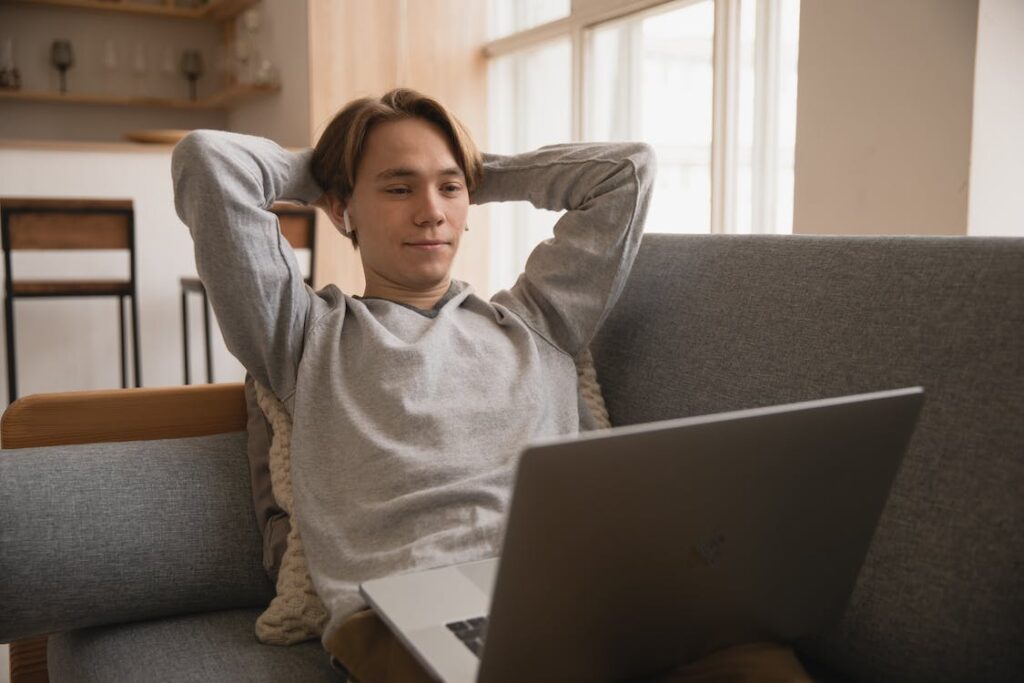Menino com os braços atrás da cabeça olhando notebook