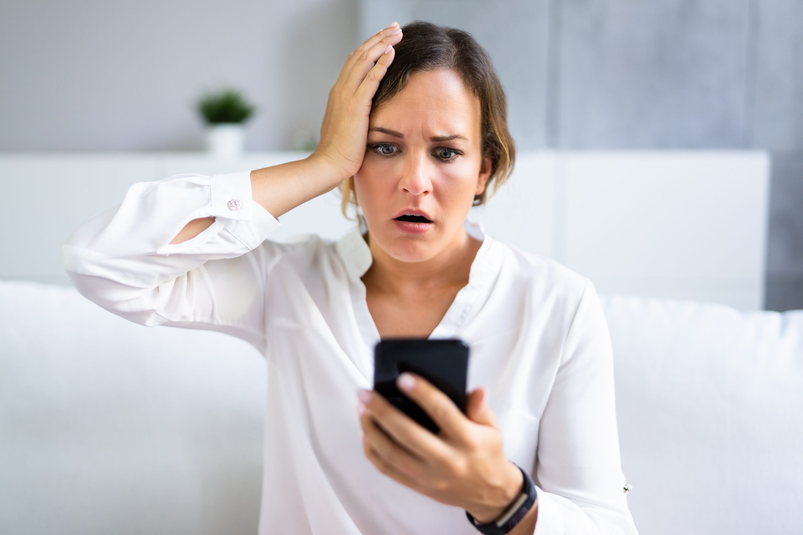 Mulher confusa com a mão na cabeça olhando celular