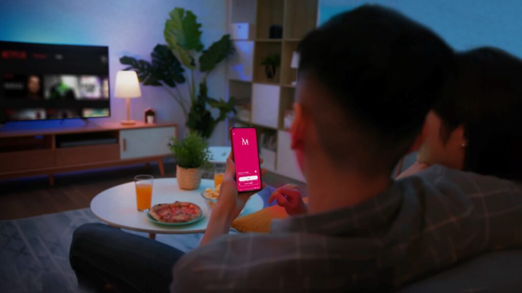 Casal assitindo TV e app do banco aberto no celular