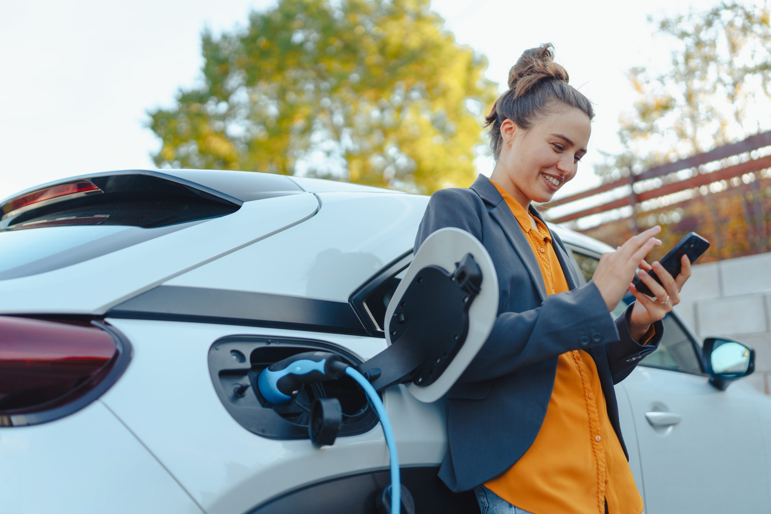 Mulher encostada em carro elétrico enquanto carrega