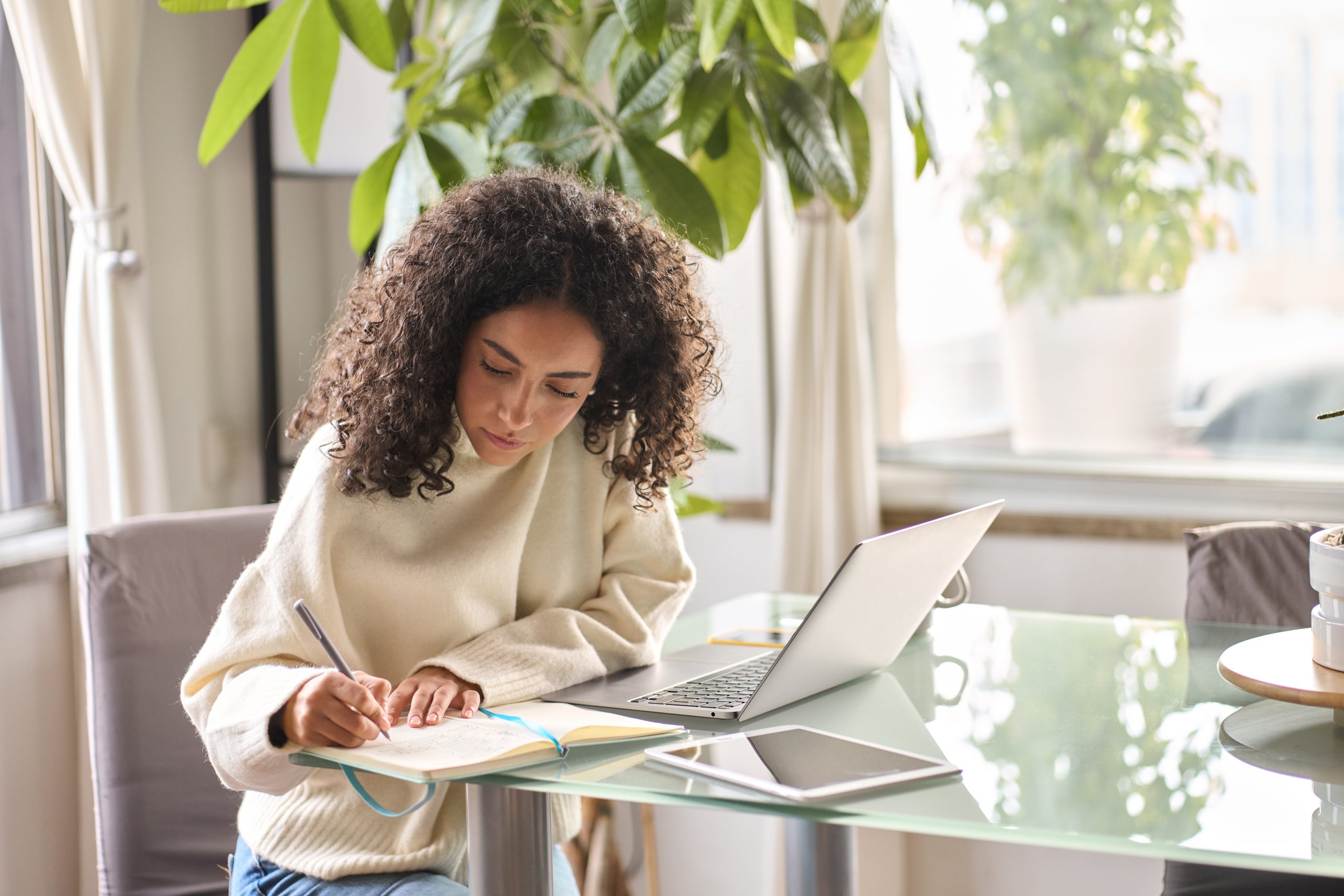 Young woman student using laptop watching online webinar writing at home.