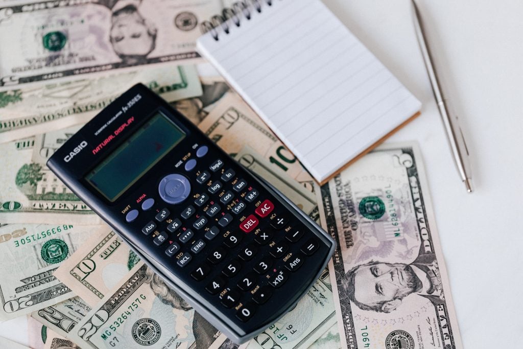 notas de dólar embaixo de calculadora e bloco de anotações