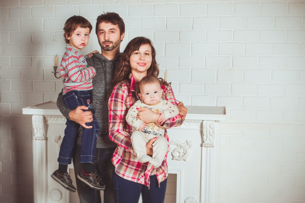 família de quatro pessoas (um casal e duas crianças) em pé atrás de móvel branco