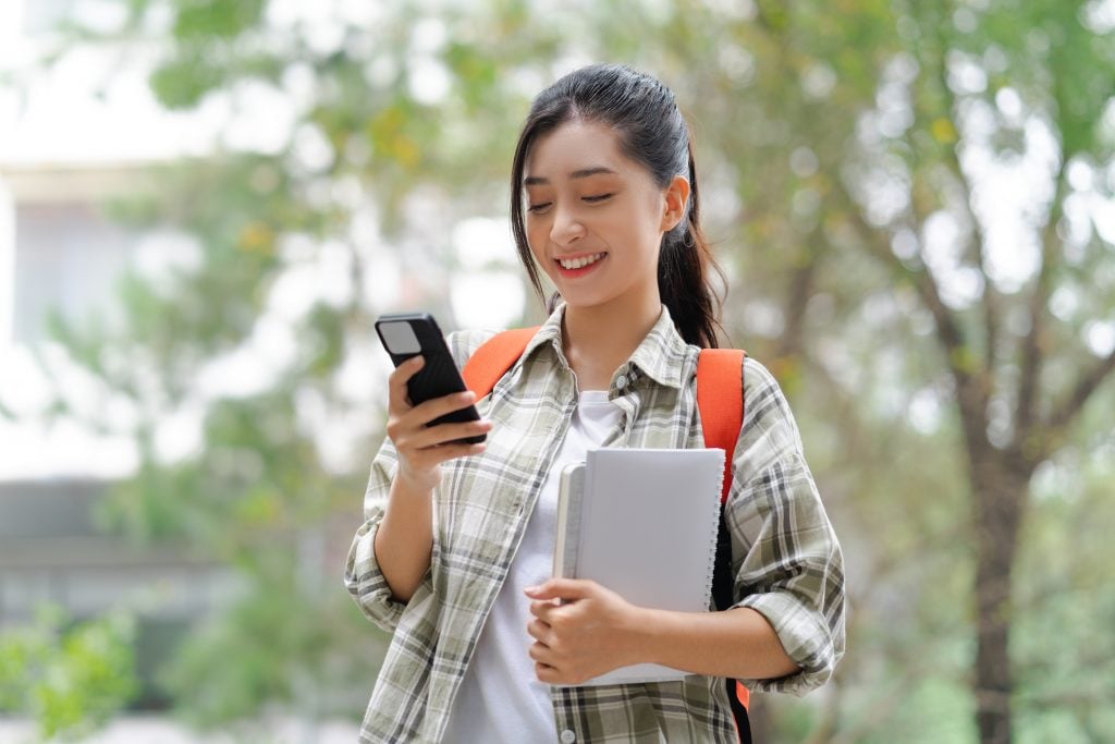 the student holds a book and uses the phone at school