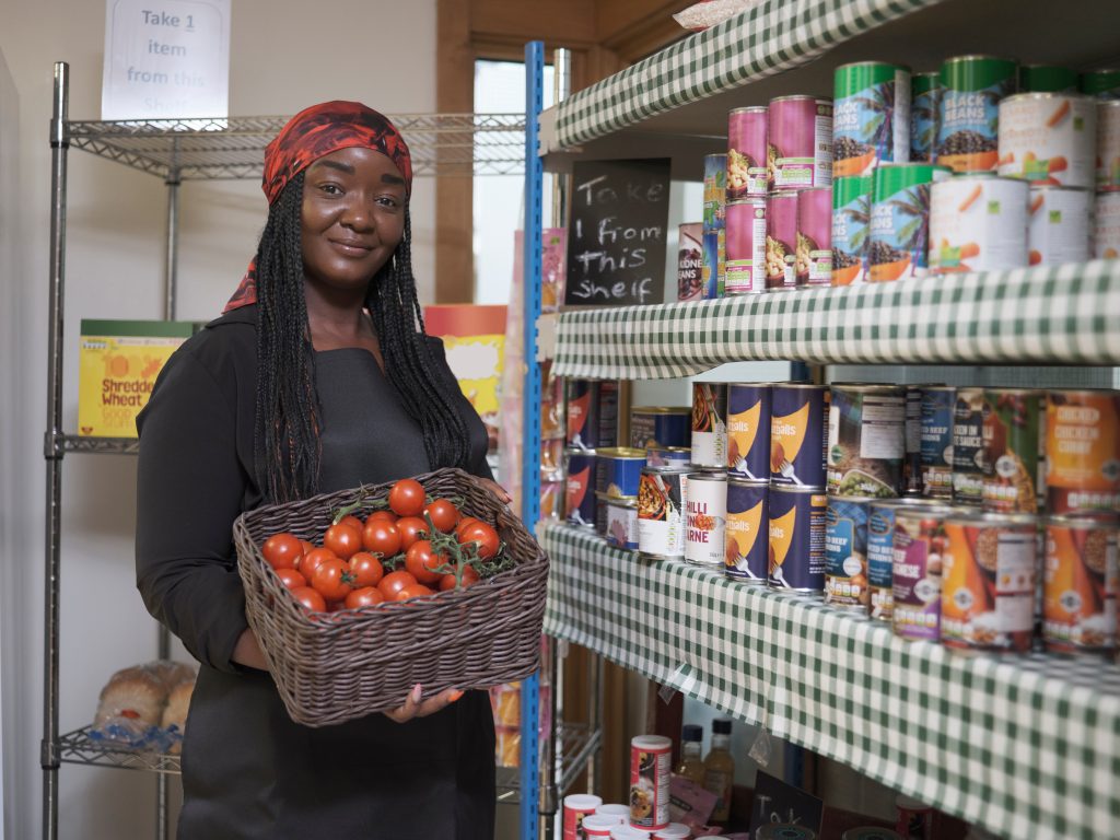 Mulher segurando cesta de tomate ao lado de prateleira de alimentos