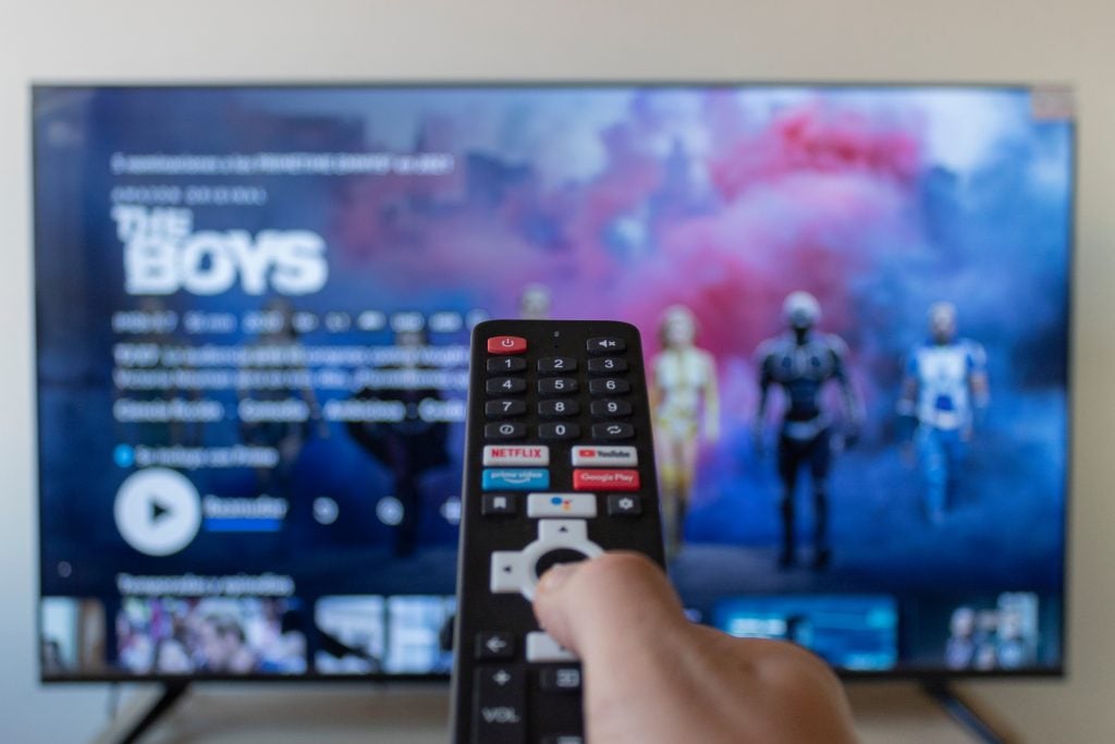 Closeup to a male right hand holding a black remote smart tv con